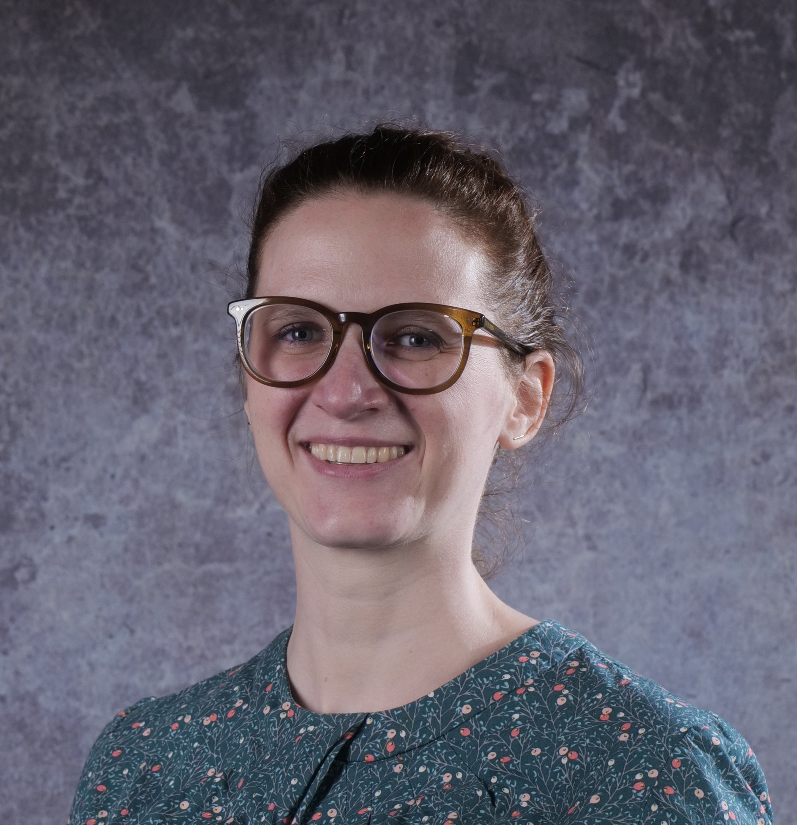 A woman wearing glasses and a green patterned shirt poses for a professional headshot. 
